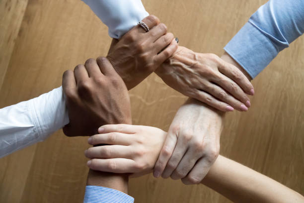 Diverse business people team connected grasping hands holding each other wrists in circle, loyalty help in teamwork concept, professional trust power support unity solidarity, close up top view above